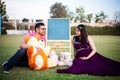 Young pregnant asian indian couple looking at each other sitting in a garden with lots teddy bear toys and blank chalkboard to Royalty Free Stock Photo