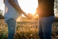 Young pregnant couple holding hands into white flowers field with the sunset and sun rays in the background Royalty Free Stock Photo