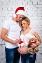 Young pregnant family with a New Year Santa hat and Christmas teddy bear