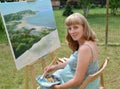 The young pregnant female artist paints a picture, sitting at an easel