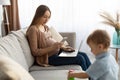 Young pregnant freelancer woman using smartphone and laptop, mom taking care of her toddler son Royalty Free Stock Photo