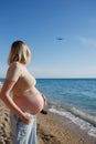 Young pregnant girl by the sea looks at a flying plane Royalty Free Stock Photo