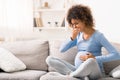 Young pregnant lady suffering with nausea, sitting on sofa