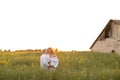 Young pregnant married couple laughs and hugs against background of blooming meadow and unfinished house in evening . Royalty Free Stock Photo