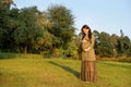 Young pregnant woman in anticipation of a baby standing in a park in the sun rays