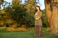 Young pregnant woman in anticipation of a baby standing in a park in the sun rays