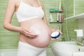 Young pregnant woman applying anti-stretch marks cream to the abdomen in the morning in the bathroom. Pregnancy, maternity and
