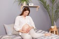 Young pregnant woman with bare belly sitting in bedroom, enjoying peaceful moment while awaiting baby's arrival Royalty Free Stock Photo