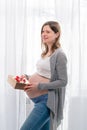 Young pregnant woman with big belly holding a gift wrapped with red ribbon, baby shower party with presents. Royalty Free Stock Photo