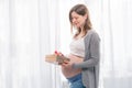 Young pregnant woman with big belly holding a gift wrapped with red ribbon, baby shower party with presents. Royalty Free Stock Photo