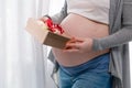 Young pregnant woman with big belly holding a gift wrapped with red ribbon, baby shower party with presents. Royalty Free Stock Photo