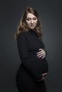 A young pregnant woman in a black tight dress touches her belly with her hands. A beautiful pensive brown-haired woman is waiting Royalty Free Stock Photo