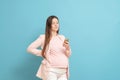 happy young pregnant woman on blue background calls by mobile phone, discharge of amniotic fluid, the beginning of labor process
