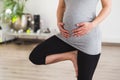 Young pregnant woman standing in tree pose doing prenatal yoga holding belly Royalty Free Stock Photo