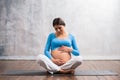 Young pregnant woman doing yoga exercises and meditating at home. Health care, mindfulness, relaxation and wellness