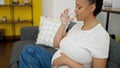 Young pregnant woman drinking glass of water sitting on sofa at home Royalty Free Stock Photo