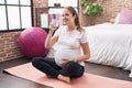 Young pregnant woman drinking water sitting on yoga mat at bedroom Royalty Free Stock Photo