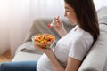 Young Pregnant Woman Eating Fresh Vegetable Salad For Lunch, Sitting On Sofa Royalty Free Stock Photo