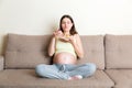 Young pregnant woman enjoys eating tasty cake resting on the sofa at home. Unhealthy diet during pregnancy concept Royalty Free Stock Photo