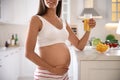 Young pregnant woman with glass of juice in kitchen, closeup. Taking care of baby health