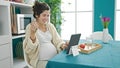 Young pregnant woman having breakfast watching video on touchpad at dinning room Royalty Free Stock Photo