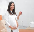 Young pregnant woman holding an Apple,standing in the kitchen Royalty Free Stock Photo