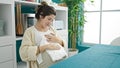 Young pregnant woman holding baby clothes sitting on table at dinning room Royalty Free Stock Photo