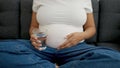 Young pregnant woman holding glass of water sitting on sofa at home Royalty Free Stock Photo