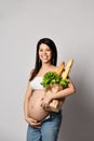 Young pregnant woman holding grocery paper shopping bag full of fresh vegetables and white bread. Diet healthy eating concept Royalty Free Stock Photo