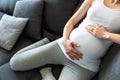 Young pregnant woman holding her belly sitting on a sofa Royalty Free Stock Photo
