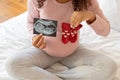 Young pregnant woman holding sonogram next to tiny red heart-patterned baby socks Royalty Free Stock Photo