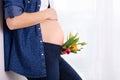 Young pregnant woman, holding tulip flowers, leaning on a wall