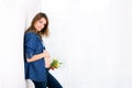 Young pregnant woman, holding tulip flowers, leaning on a wall