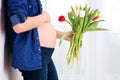 Young pregnant woman, holding tulip flowers, leaning on a wall