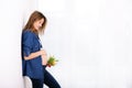 Young pregnant woman, holding tulip flowers, leaning on a wall