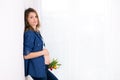 Young pregnant woman, holding tulip flowers, leaning on a wall