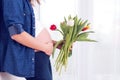 Young pregnant woman, holding tulip flowers, leaning on a wall