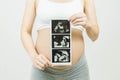 A young pregnant woman holding ultrasound images over grey background.Concept of pregnancy, health care, gynecology, medicine.