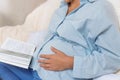 young pregnant woman holds her hand on her stomach and reads a book. depersonalizacia