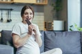 Young pregnant woman at home sitting on the couch eating chocolate Royalty Free Stock Photo