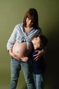 Young pregnant woman hugs her eldest son, mom and son put their hands on big belly