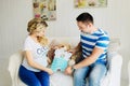 Young pregnant woman with husband on white sofa in room looking at baby clothes. Royalty Free Stock Photo