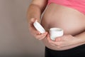 Young pregnant woman keeps skin cream care close to her belly Royalty Free Stock Photo
