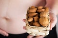 Young pregnant woman keeps woven mini basket full of nuts