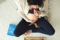 Young pregnant woman, lying in bed with smartphone, book, coffee