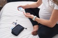 Young pregnant woman measuring glucose sitting on bed at bedroom Royalty Free Stock Photo