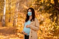 Young pregnant woman in medical mask on walk at autumn park during coronavirus epidemic Royalty Free Stock Photo