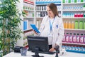 Young pregnant woman pharmacist smiling confident using computer and touchpad at pharmacy