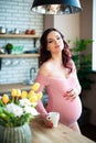 Young pregnant woman in pink bodysuit drinking water in the kitchen. How to get rid of morning sickness and toxemia. Drugs and Royalty Free Stock Photo