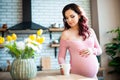 Young pregnant woman in pink bodysuit drinking water in the kitchen. How to get rid of morning sickness and toxemia. Drugs and Royalty Free Stock Photo